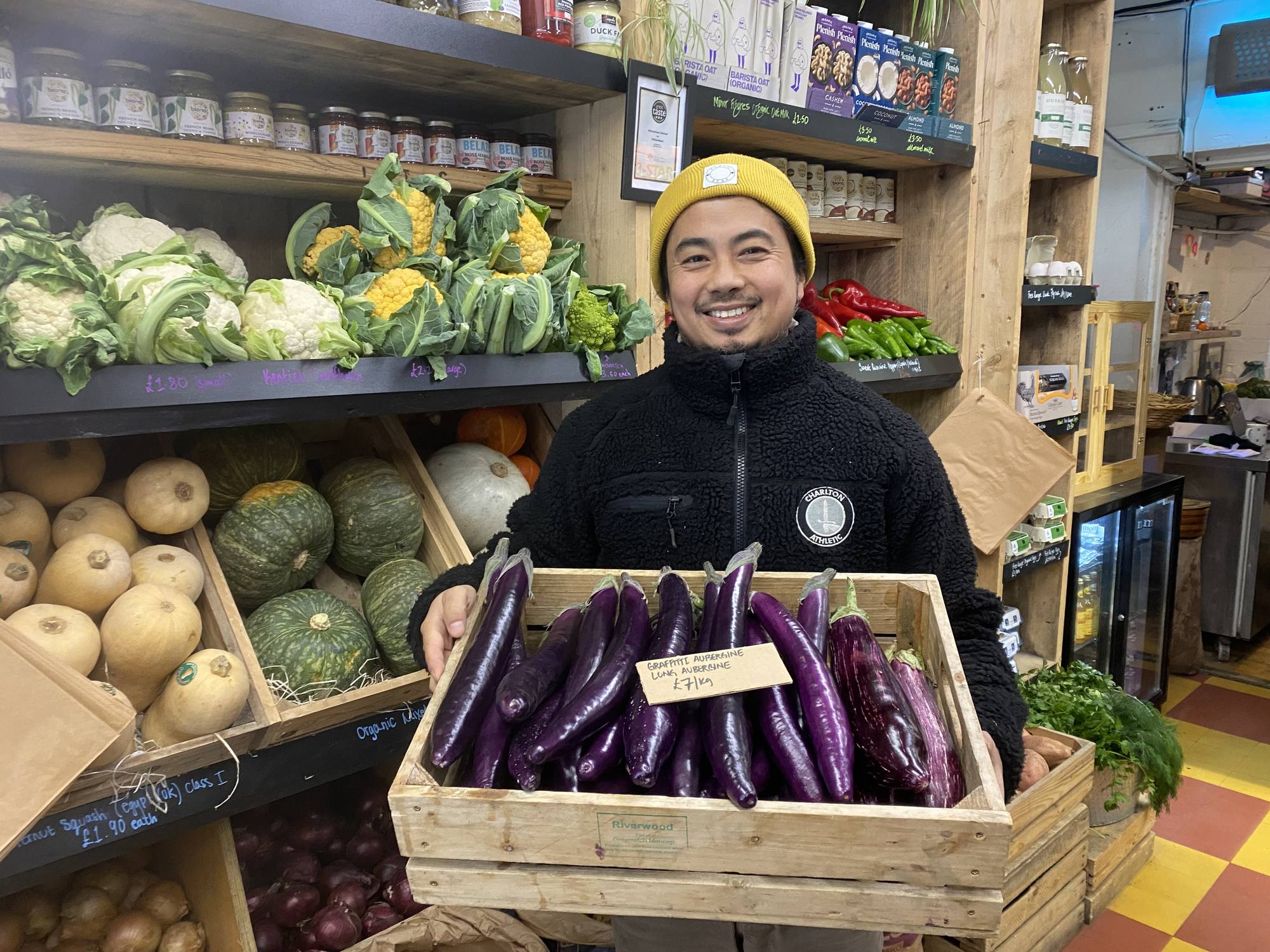 Bardan Pradhan, owner of The Village Greengrocers, holding a crate of graffiti aubergines in the shop